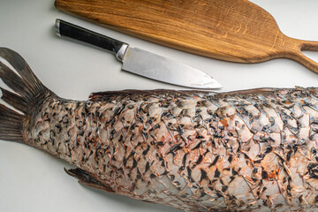 Gutted carp fish, headless on a white table with a cutting board and a knife.