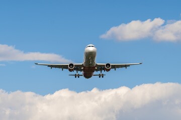 Airplane approaches landing surrounded by fluffy clouds in clear blue sky during bright daylight...