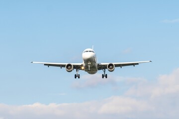 Commercial airplane approaches runway at sunny day with clear skies and few clouds in the background