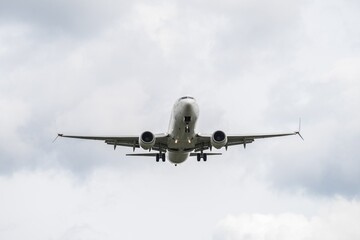 Commercial airplane approaches runway in cloudy sky over urban landscape at midday for landing