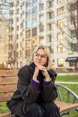 A woman sits contemplatively on a bench outside. Woman in the city.