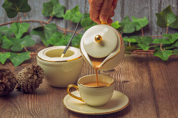 Indian masala chai tea. Masala chai spiced tea with milk and spices or karak chai or cutting chai. Tea being poured into ceramic glasses from a tea pot and spices on isolated background. 