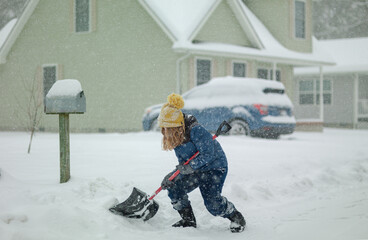 Funny Kid removing snow with a shovel in the yard on snowy winter day. Child clearing sidewalks and...