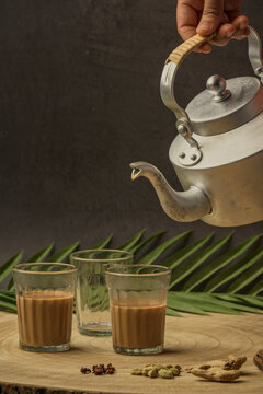 Indian masala chai tea. Masala chai spiced tea with milk and spices or karak chai or cutting chai. Tea being poured into glasses from a kettle and spices on isolated background.