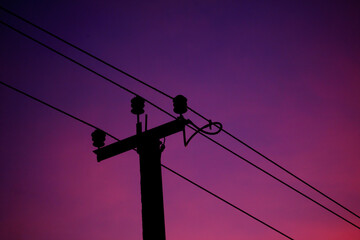 A power line pole is silhouetted against a purple sky