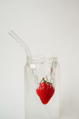 Fresh strawberry splashing into water in a glass with a reusable