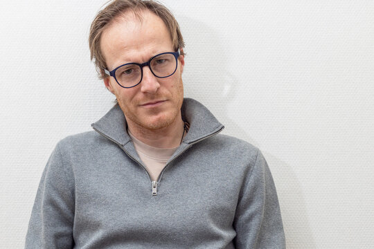 man with glasses leans against the wall while smiling softly
