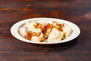 Delicious dumplings topped with crispy pork pieces on wooden table Savory vegetable pie served with...