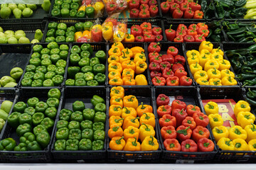 Green, orange, yellow and red bell peppers on a supermarket shelf