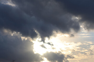 Dense gray clouds and bright last sun lays with white clouds around