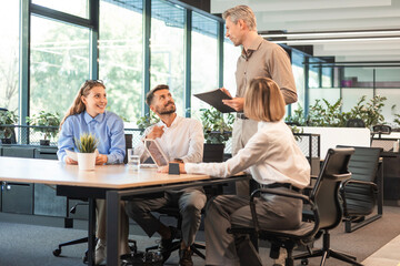 Handsome man gesturing and discussing something while his coworkers listening to him sitting at the office table.