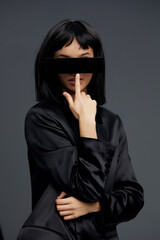 Woman in black suit with blindfold and hand over mouth, symbolizing secrecy, mystery, or being silenced, standing against a dark background