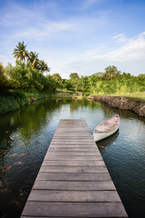 long wooden bridge extending into a calm river with boats and schools of beautiful koi fish