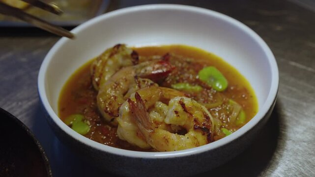 human hand with metal tongs, adding one shrimp to a white bowl of Spicy prawn rougaille on table