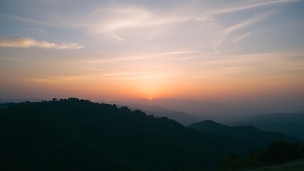 Obraz premium Serene sunset over rolling hills and mountains, painting the sky with warm orange and pink hues, a peaceful landscape.