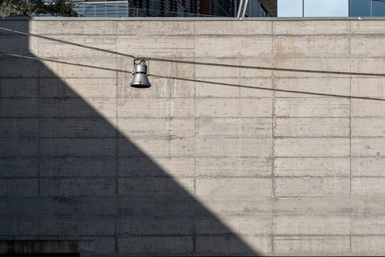 An industrial concrete wall is beautifully lit by a metallic hanging light fixture, casting a sharp shadow that highlights the textural qualities of the material.
