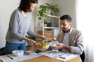 Woman serving pasta salad to husband. Married couple having meal together at home dining table.