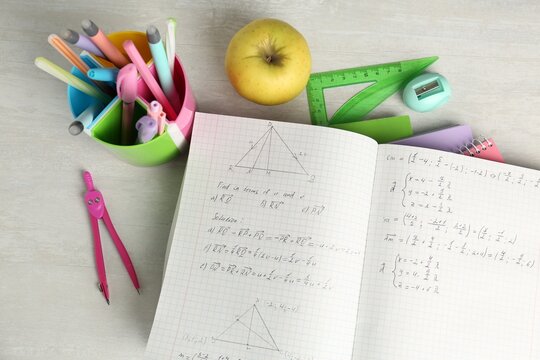 Doing homework. Notebook with math assignment, apple and stationery on white desk, flat lay
