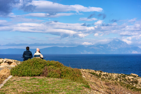 Couple sit on chairs looking at the greek coast cliff landscape