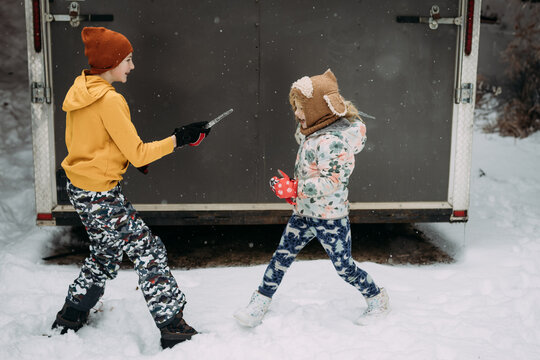 Sibling children pretending to sword fight with icicles in snow
