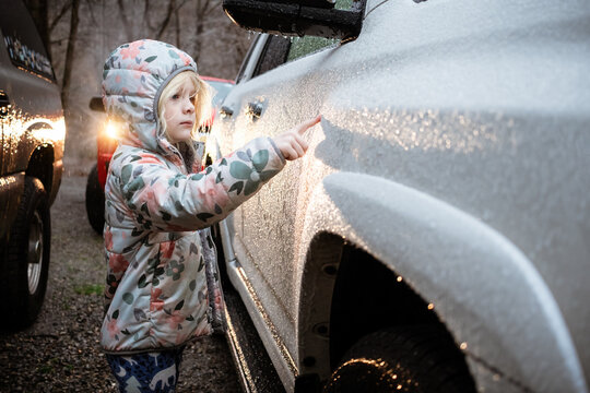 Child writing in raindrops on family car in driveway