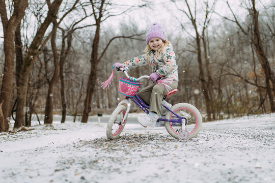 Smiling child riding bicycle in snowy rural driveway