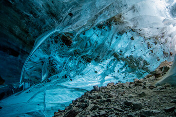 Vibrant blue ice walls inside a glacier cave with rocky floor