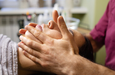 woman is getting a massage on her face. The man is gently massaging her face with his hands. The woman is relaxed and comfortable