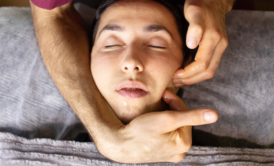 woman is getting a massage on her face. The man is gently massaging her face with his hands. The woman is relaxed and comfortable