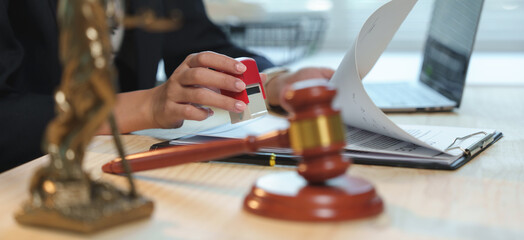 Female lawyer stamping a legal document with a judge's gavel, featuring a themis statue in the foreground, representing the ideals of justice and the legal system