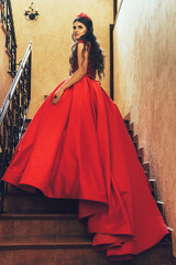 girl standing on the threshold. She is wearing a long, fluffy red off-the-shoulder dress. She has...