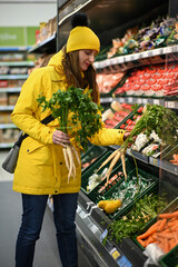 Customer selecting fresh vegetables from refrigerated shelves in grocery store