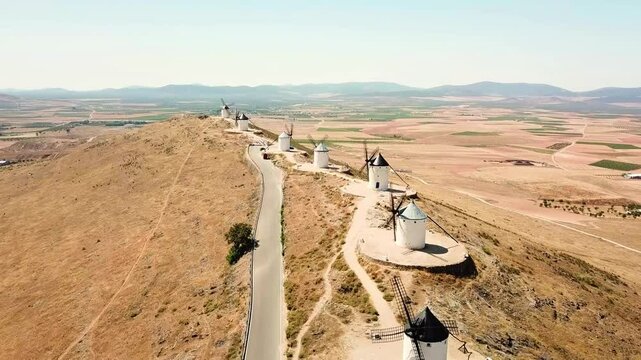 Aerial view of the iconic Molinos de Viento de Consuegra, Spain, perched along a ridge overlooking expansive fields and scenic countryside, highlighting their historic and cultural significance