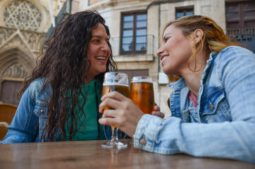 Lesbian couple smiling and toasting with beer glasses in outdoor pub on valentine's day