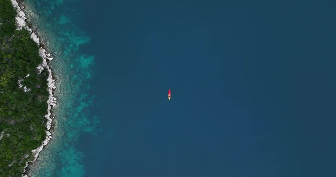 A lone kayak floats on deep blue water near Mljet's rocky green coastline, evoking serenity