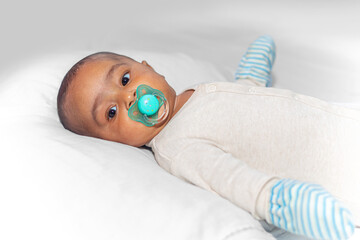 Portrait of a three-month-old baby lying down with a winter romper, hat, gloves, and a pacifier in...
