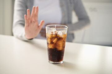 A person makes a hand gesture to refuse a glass of soda with ice. This concept highlights healthy choices, avoiding sugary drinks, weight loss, healthy lifestyle, and self-control.