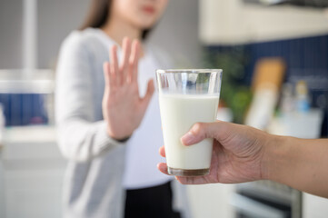 Allergy dairy food lactose intolerance allergen health care illness concept. Selective focus on a glass of milk with blurred woman gesturing refusing stop or reject say no to cow milk.