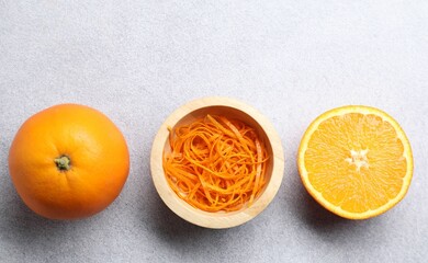 Fresh orange zest in bowl, whole and cut fruits on grey textured table, flat lay. Space for text