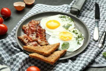 Tasty fried eggs, bacon and pieces of toast served on black table, closeup