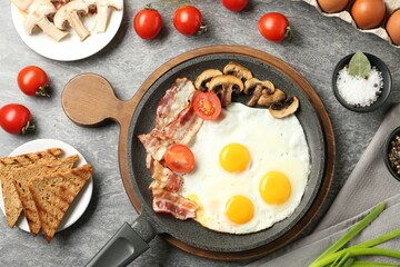 Tasty fried eggs with bacon and mushrooms served on grey table, flat lay