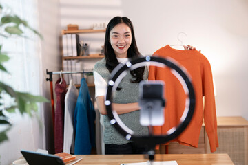 Young asian woman business owner selling clothes live streaming on mobile phone at home.