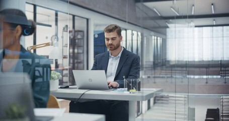 Proactive Caucasian Manager Sitting Behind a Desk, Working on Laptop Computer in Office with Diverse Colleagues. Young Male Specialist Adapts Strategies to Achieve Corporate Marketing Goals