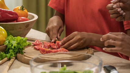 African American mother and little son preparing healthy meal, close up shot of boy holding knife and cutting tomatoes for salad, mom helping.