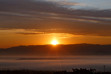 Sunrise over Misty Mountains, A breathtaking sunrise paints the sky in vibrant hues of orange and gold as the sun rises majestically behind a range of misty mountains.