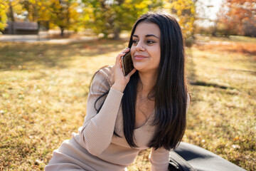 Fototapeta premium Young woman talking on smartphone in autumn park
