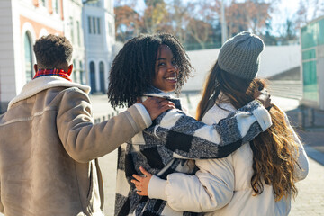 Three happy young students walking together embracing each other in the city