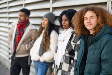 Group of diverse young people leaning against metal wall in winter