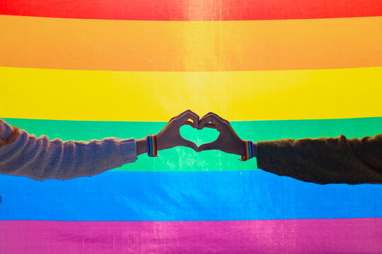 Two people making heart shape with hands and rainbow flag