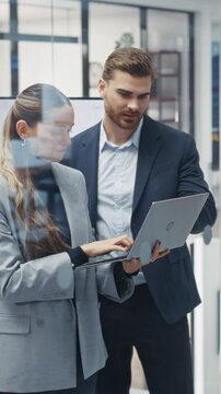 Vertical Screen: Young Coworkers Planning Next Business Steps in a Team Meeting, Using a Laptop Computer to Assign Responsibilities. Caucasian Male and Female Using a Project Management Online Tool